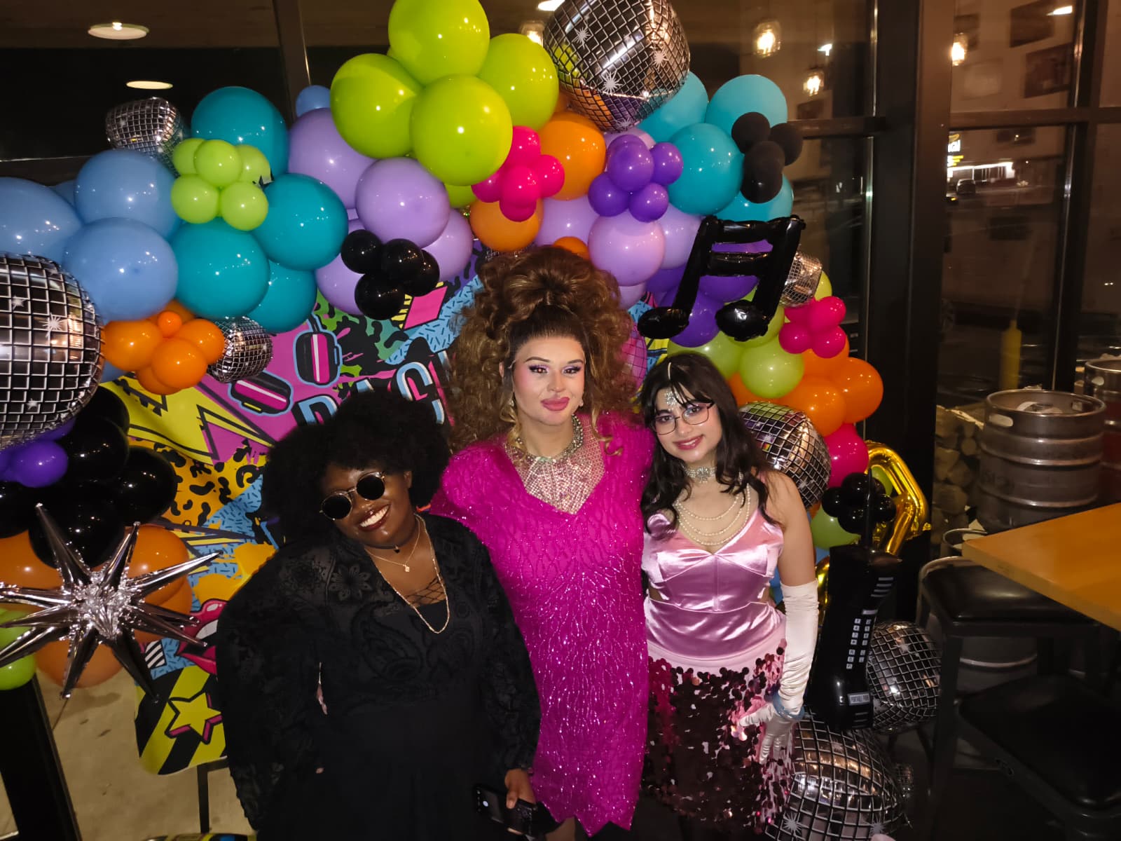 3 people dressed up fancy infront of balloons